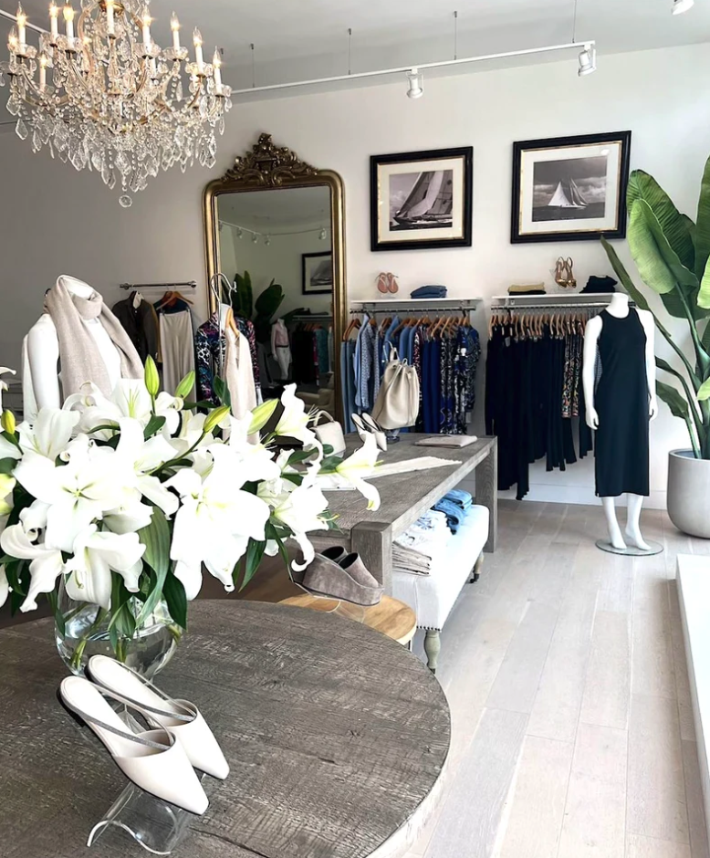 Elegant boutique interior with crystal chandelier, clothing racks, ornate mirror, and white lilies.