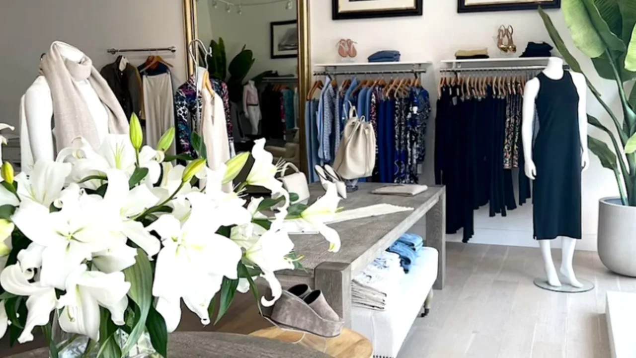 Elegant boutique interior with crystal chandelier, clothing racks, ornate mirror, and white lilies.