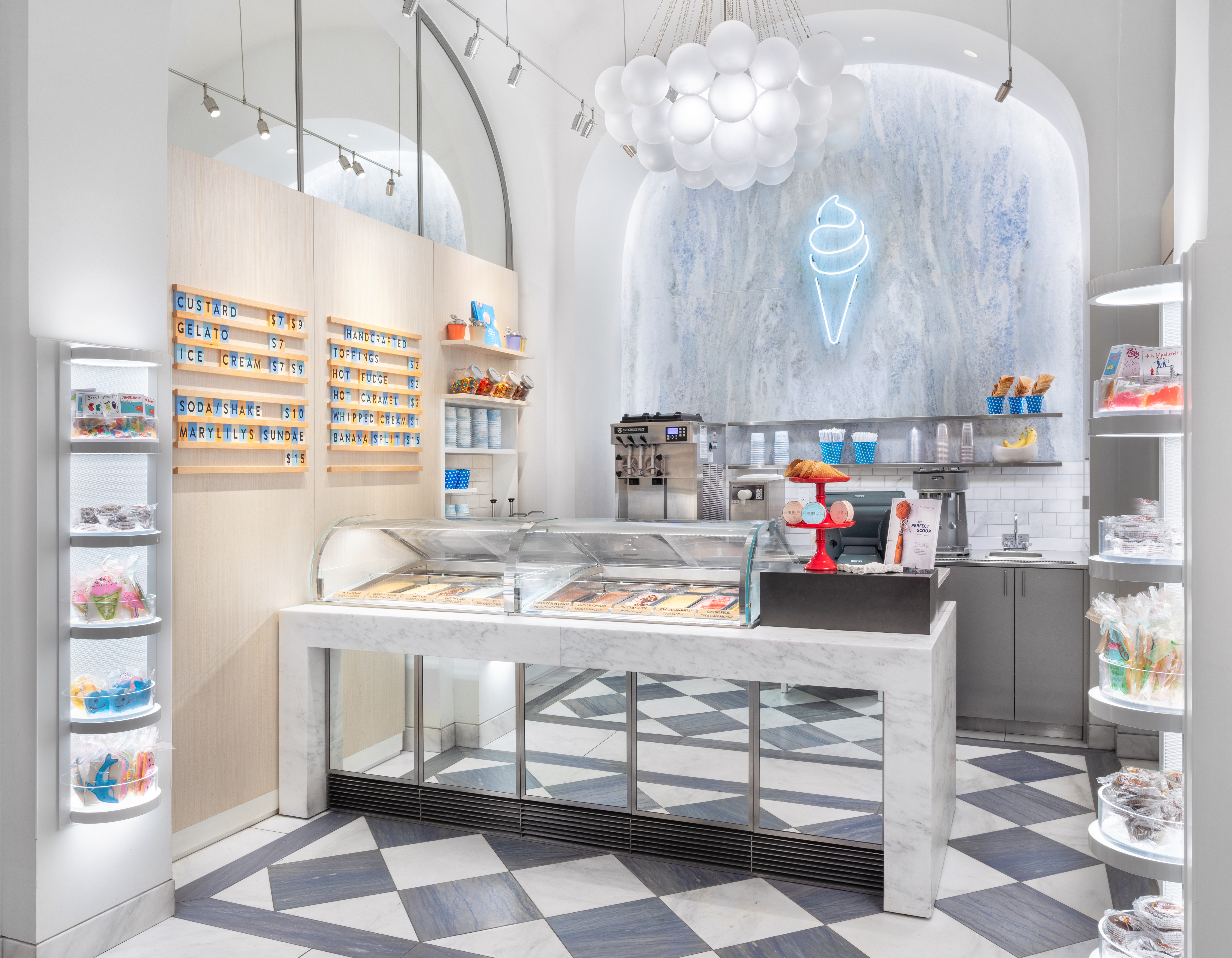 Modern ice cream shop interior with white and blue decor, neon cone sign, menu boards, and display cases.