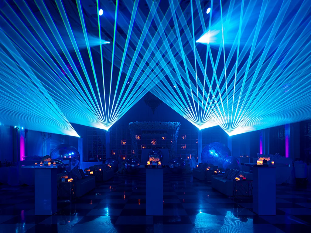 Nightclub-style event space with a checkered dance floor, mirrored disco spheres and blue laser beams sweeping the ceiling over lounge seating.