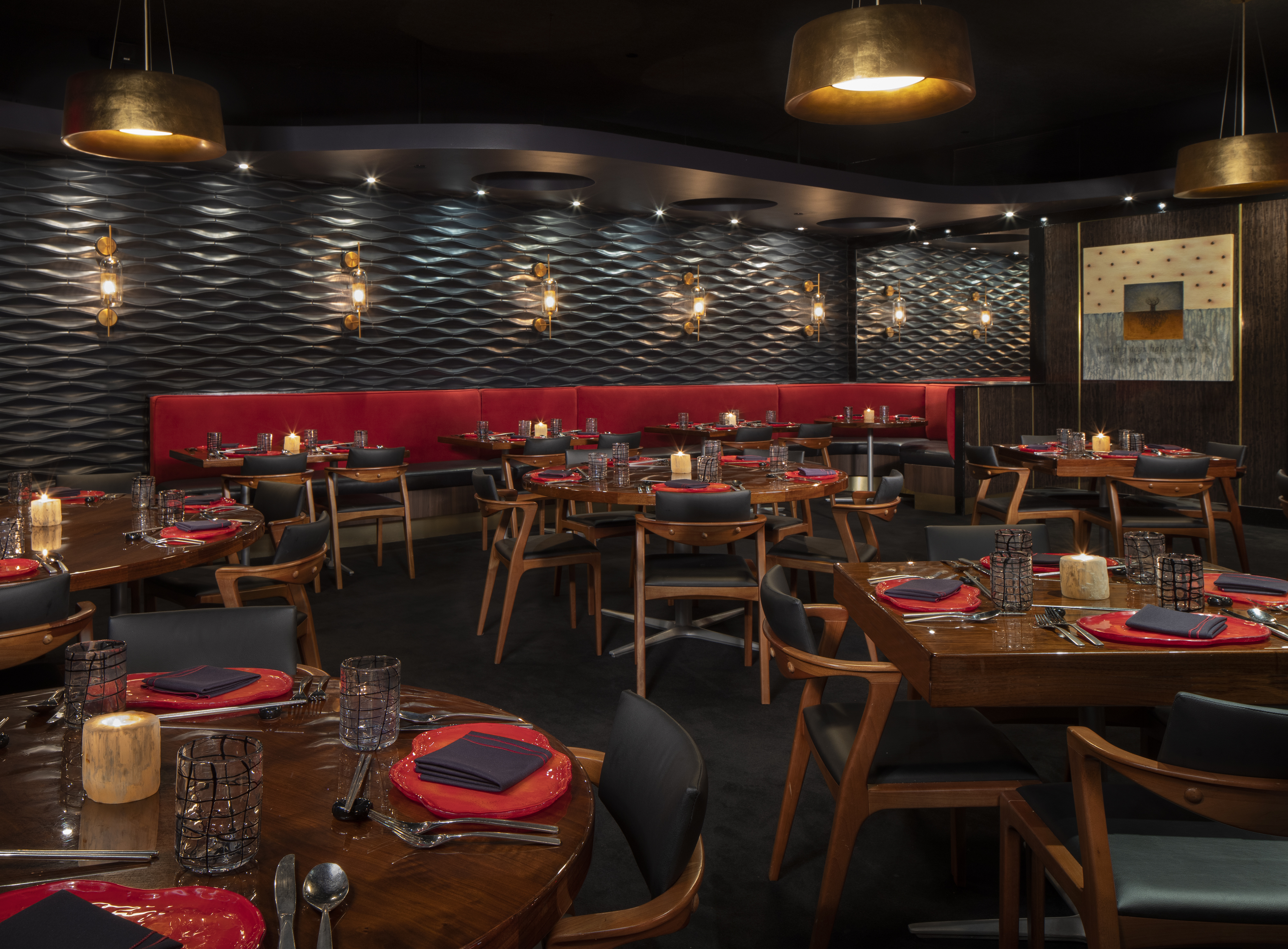 Modern restaurant interior with textured walls, gold pendant lights, red banquette seating, and tables.