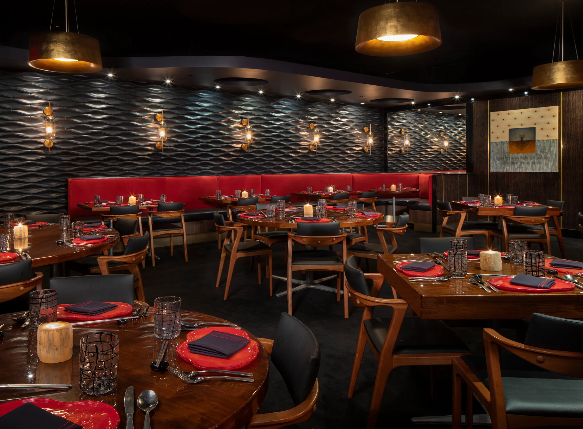 Modern restaurant interior with textured walls, gold pendant lights, red banquette seating, and tables.