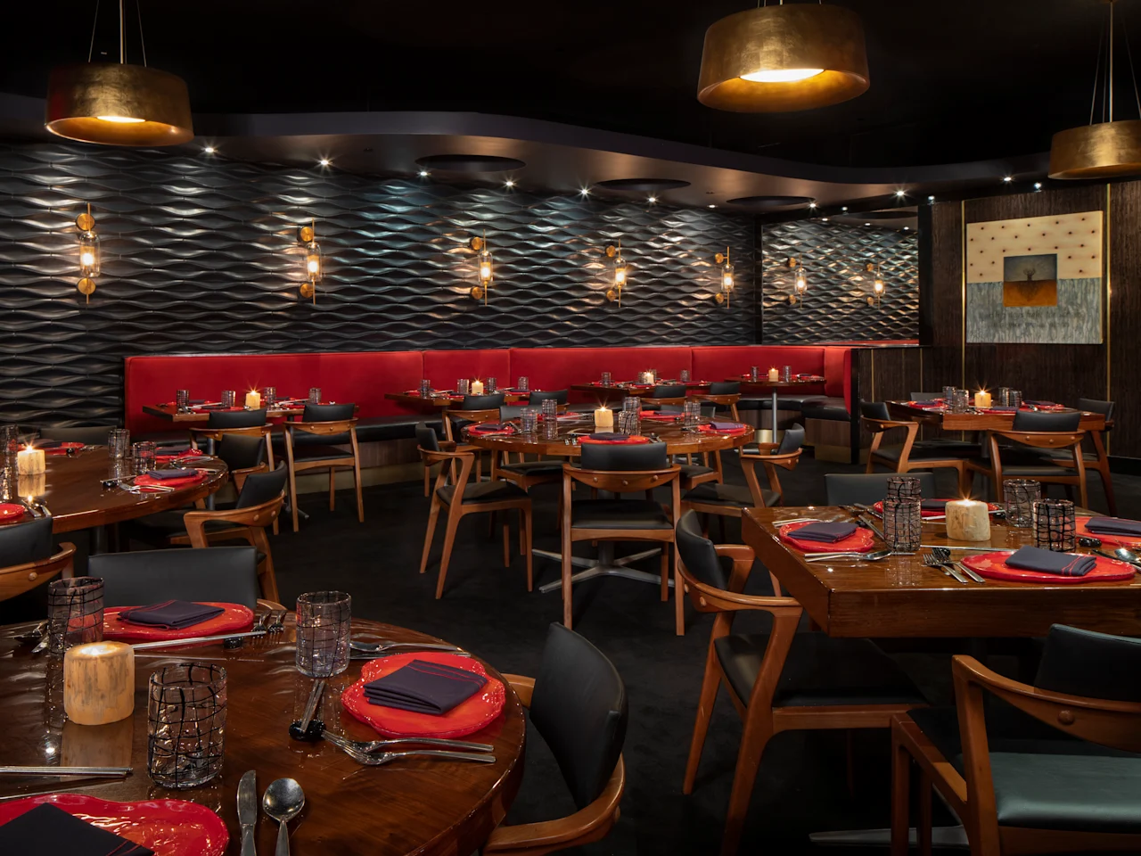 Modern restaurant interior with textured walls, gold pendant lights, red banquette seating, and tables.