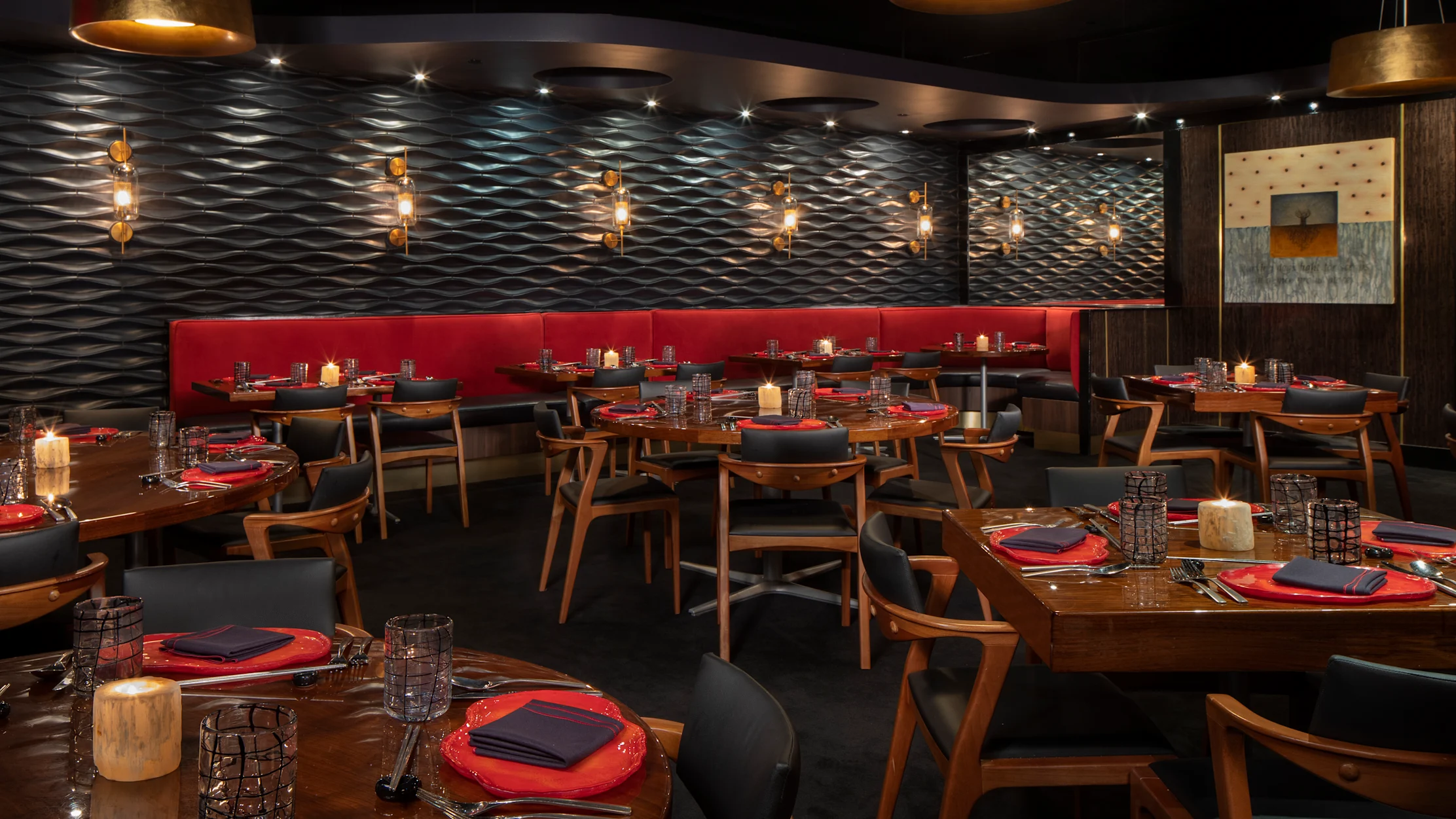 Modern restaurant interior with textured walls, gold pendant lights, red banquette seating, and tables.