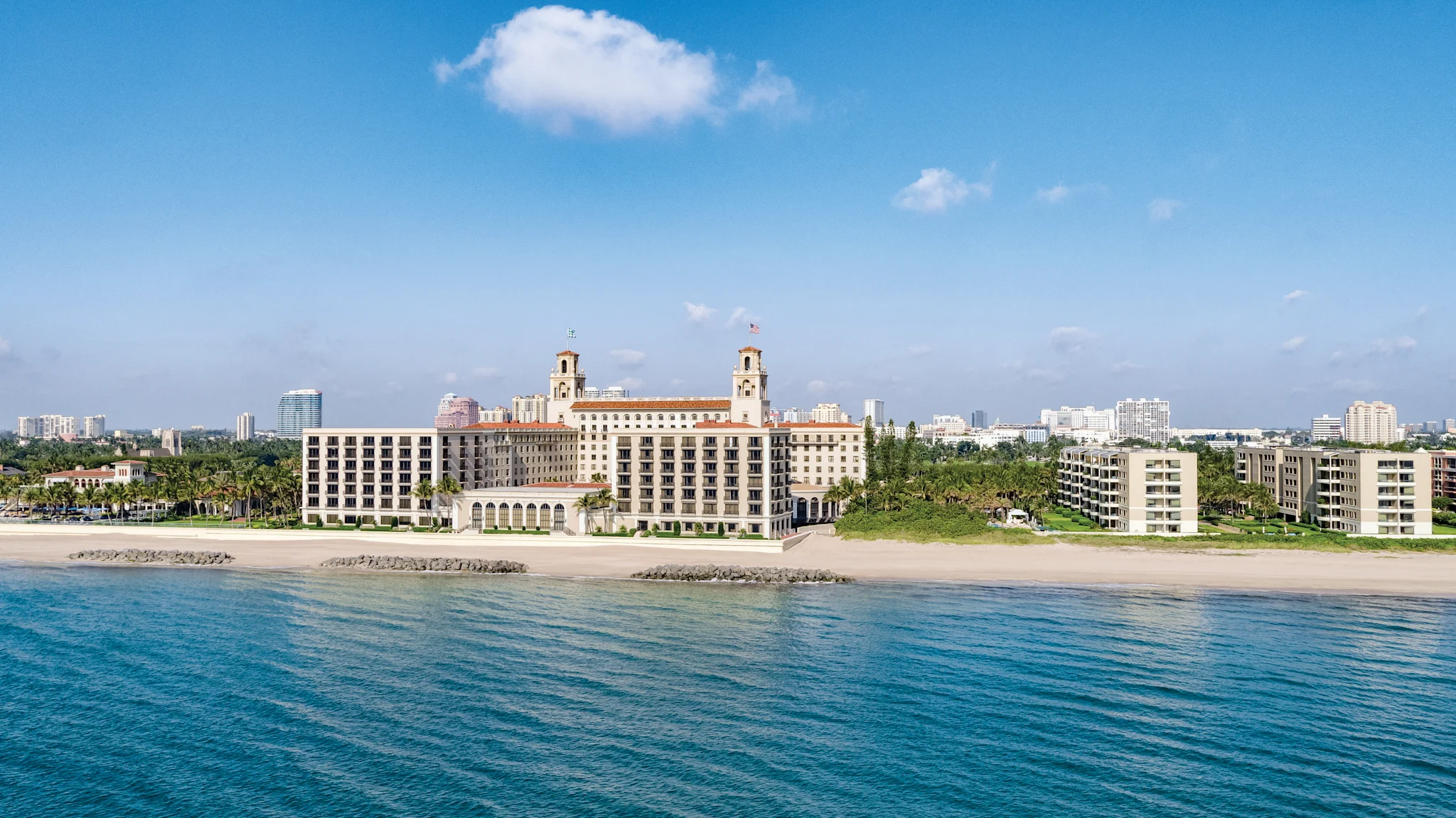 Beachfront view of The Breakers Palm Beach hotel with twin towers and terracotta roof viewed from turquoise ocean waters.
