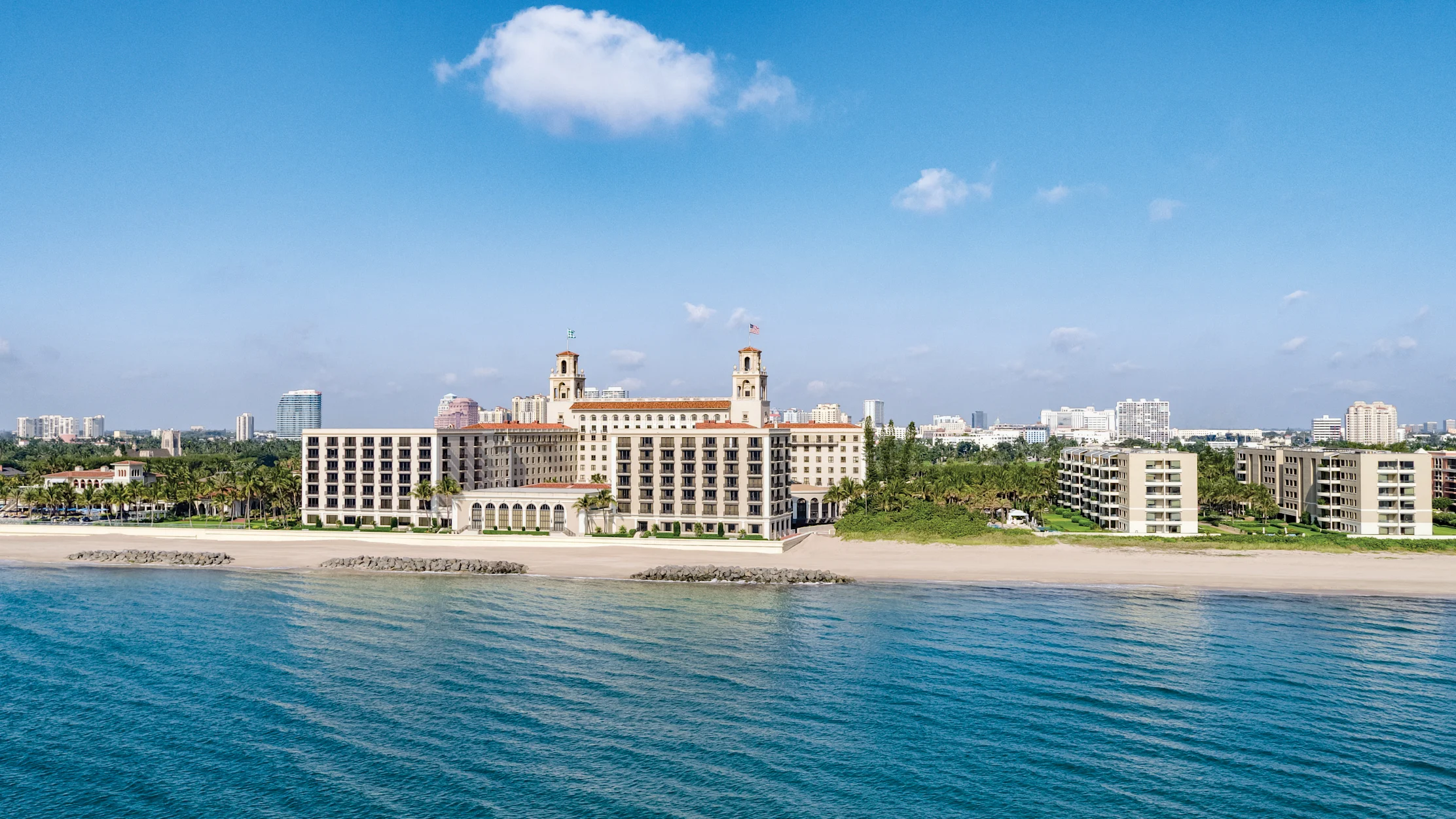 Beachfront view of The Breakers Palm Beach hotel with twin towers and terracotta roof viewed from turquoise ocean waters.