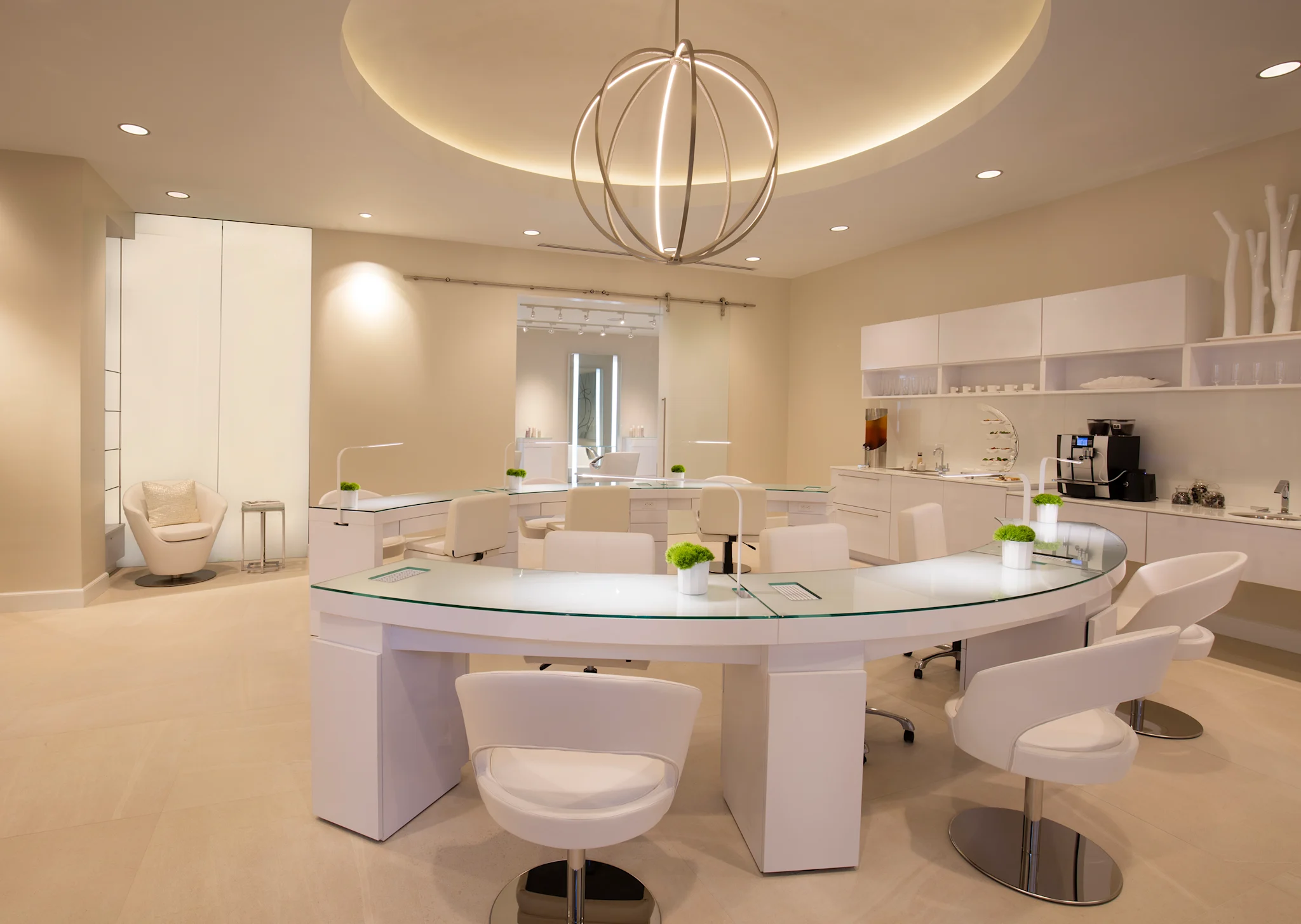 Modern white nail salon interior with curved manicure stations, spherical pendant light, and beige walls.