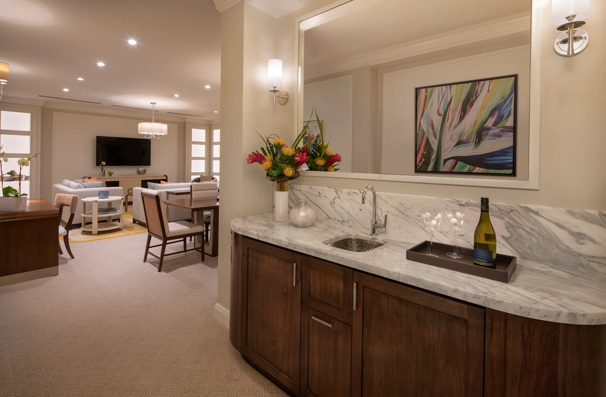 Elegant wet bar with marble countertop and wood cabinets, tropical flowers, wine glasses, and artwork.