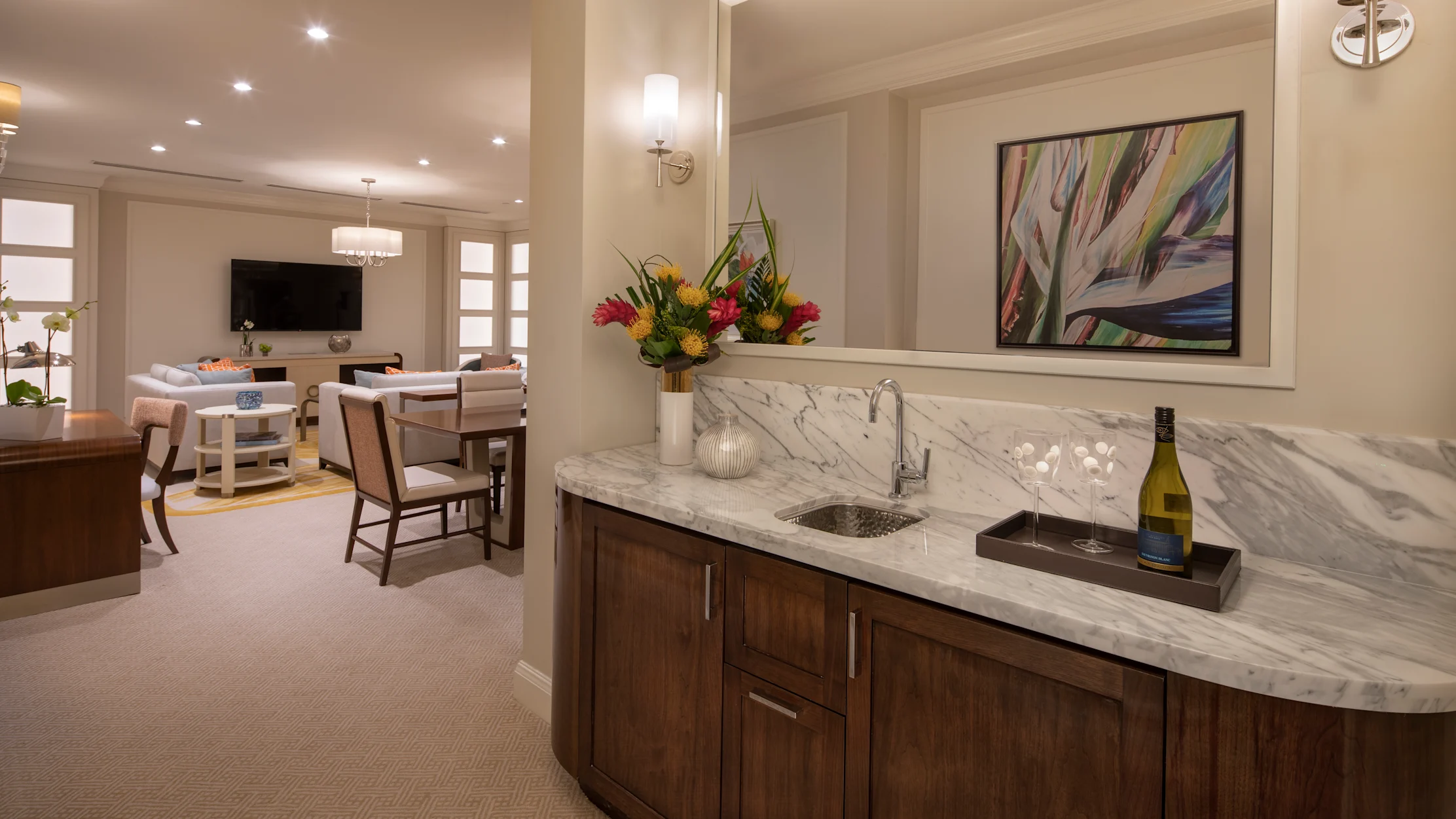 Elegant wet bar with marble countertop and wood cabinets, tropical flowers, wine glasses, and artwork.