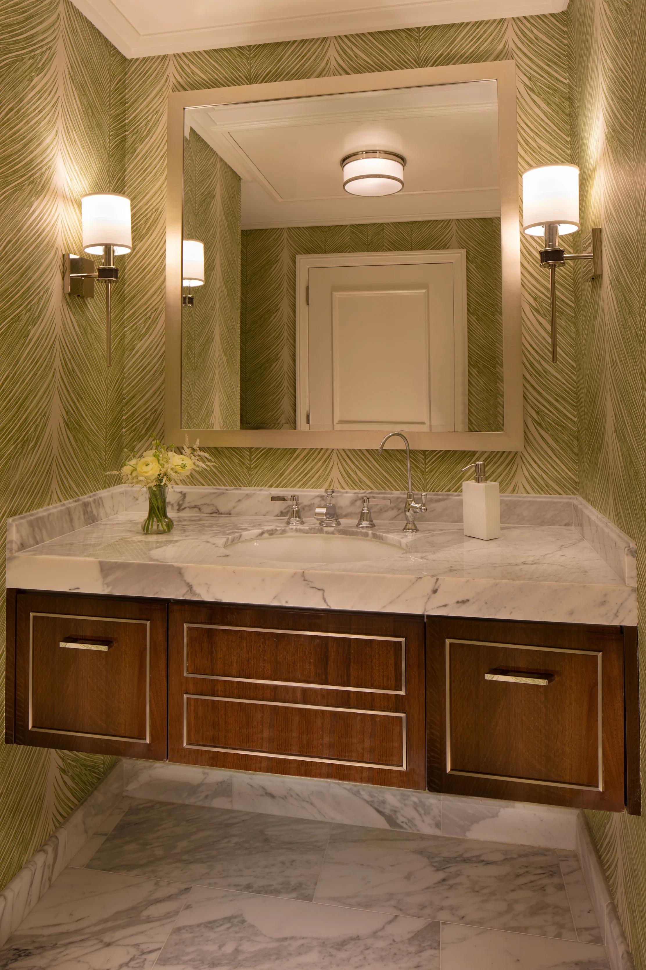 Elegant bathroom with green chevron wallpaper, marble vanity, dark wood cabinets, and wall sconces.