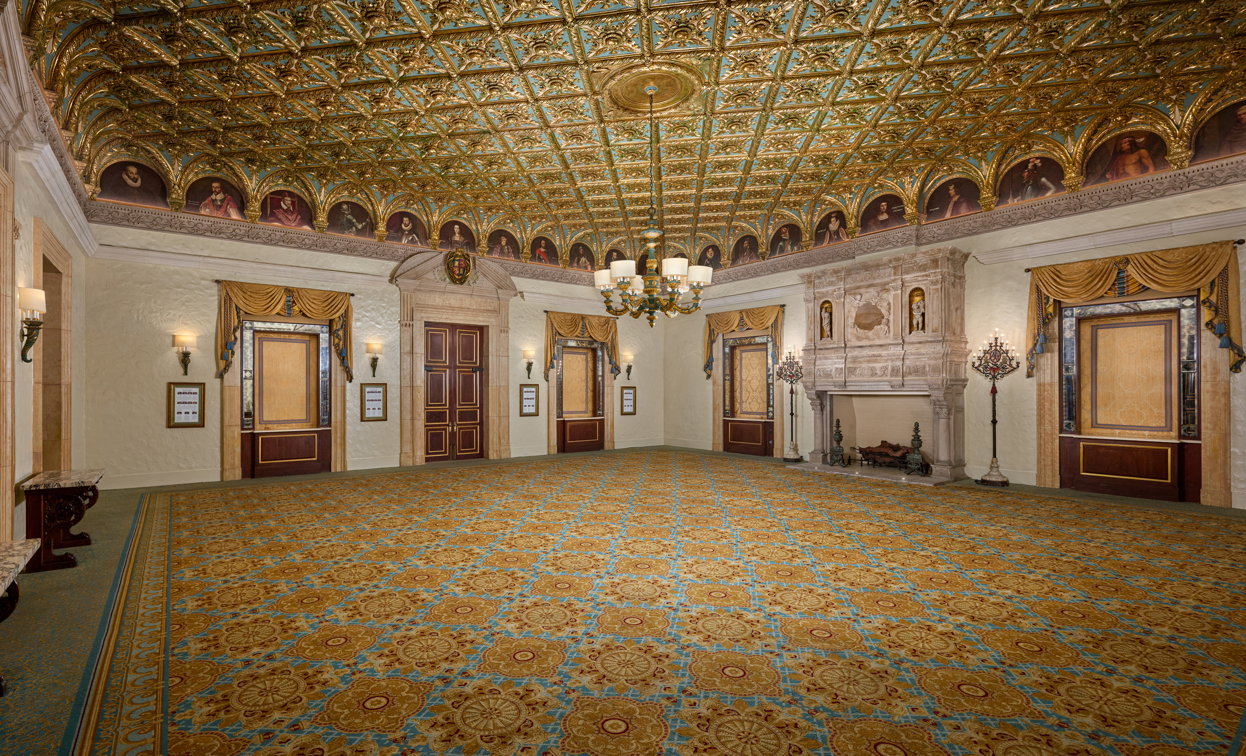 Ornate ballroom with gold and turquoise ceiling, patterned carpet, chandelier, and elegant doors.
