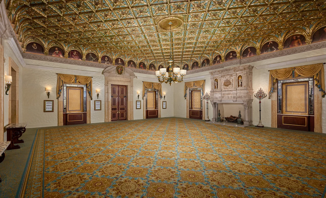 Ornate ballroom with gold and turquoise ceiling, patterned carpet, chandelier, and elegant doors.