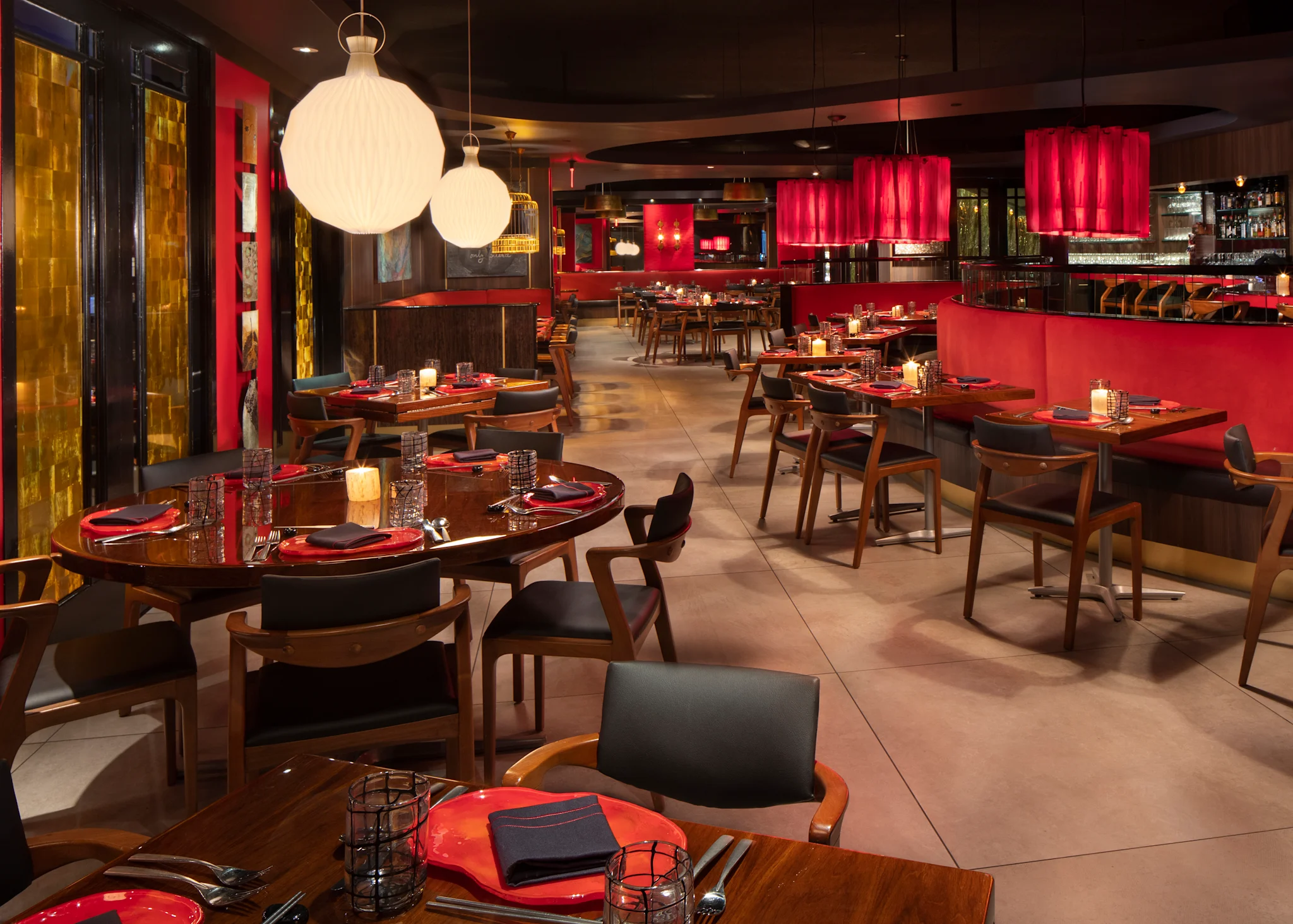 Modern restaurant interior with red accents, wooden tables, black chairs, and white globe pendant lights.