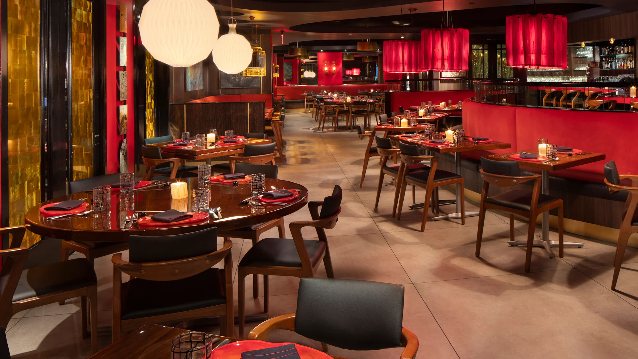 Modern restaurant interior with red accents, wooden tables, black chairs, and white globe pendant lights.