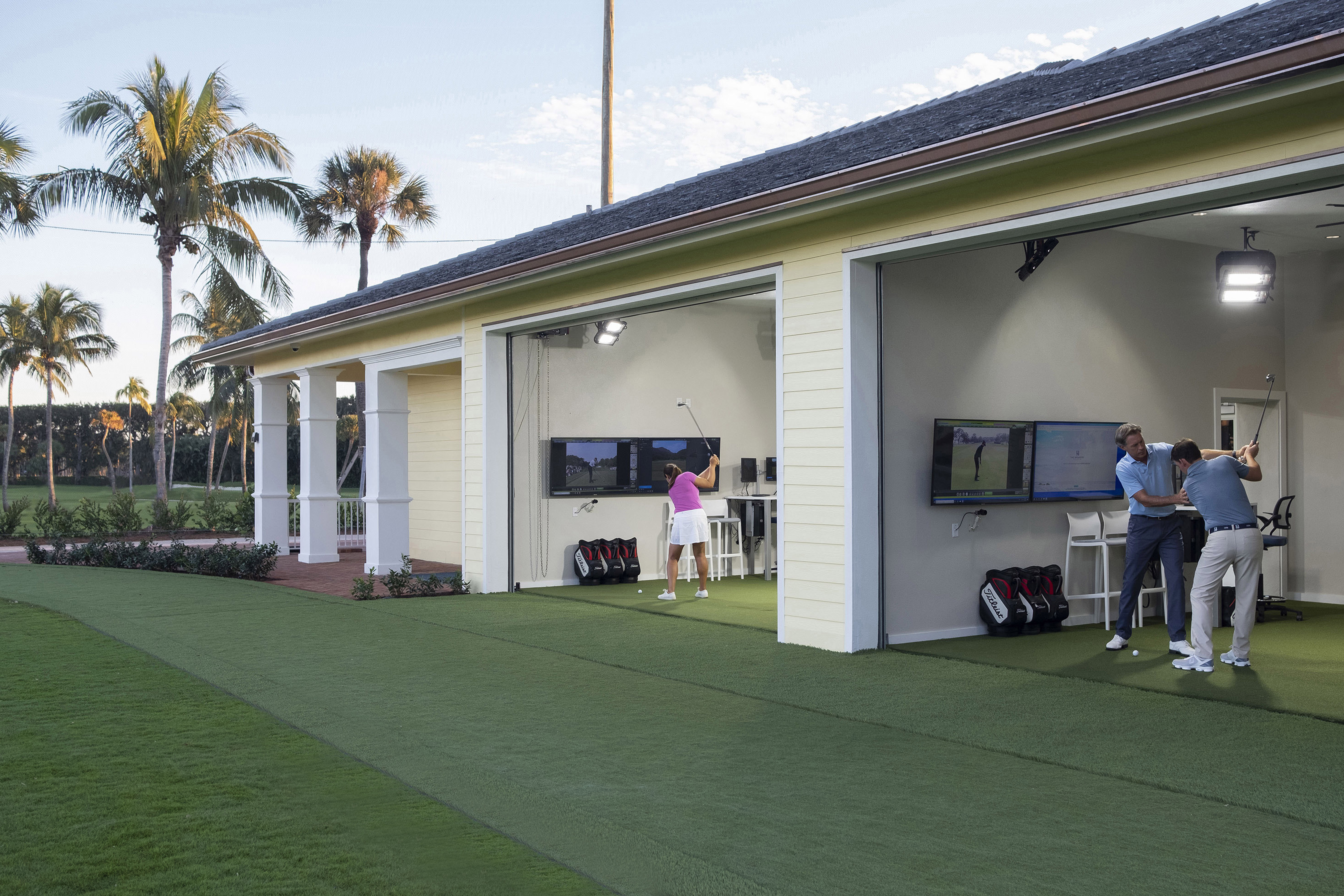 Golfers practicing at outdoor simulator bays with screens and palm trees in background.
