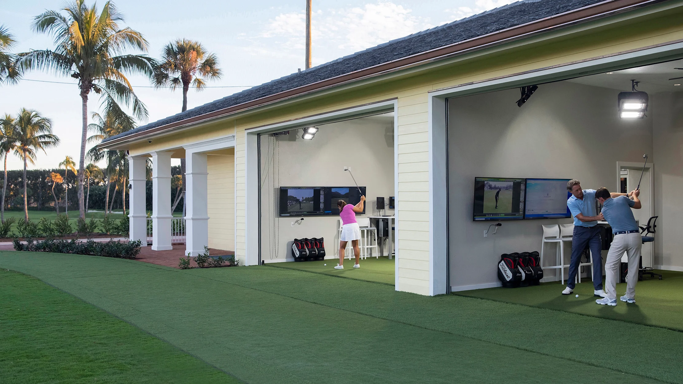 Golfers practicing at outdoor simulator bays with screens and palm trees in background.
