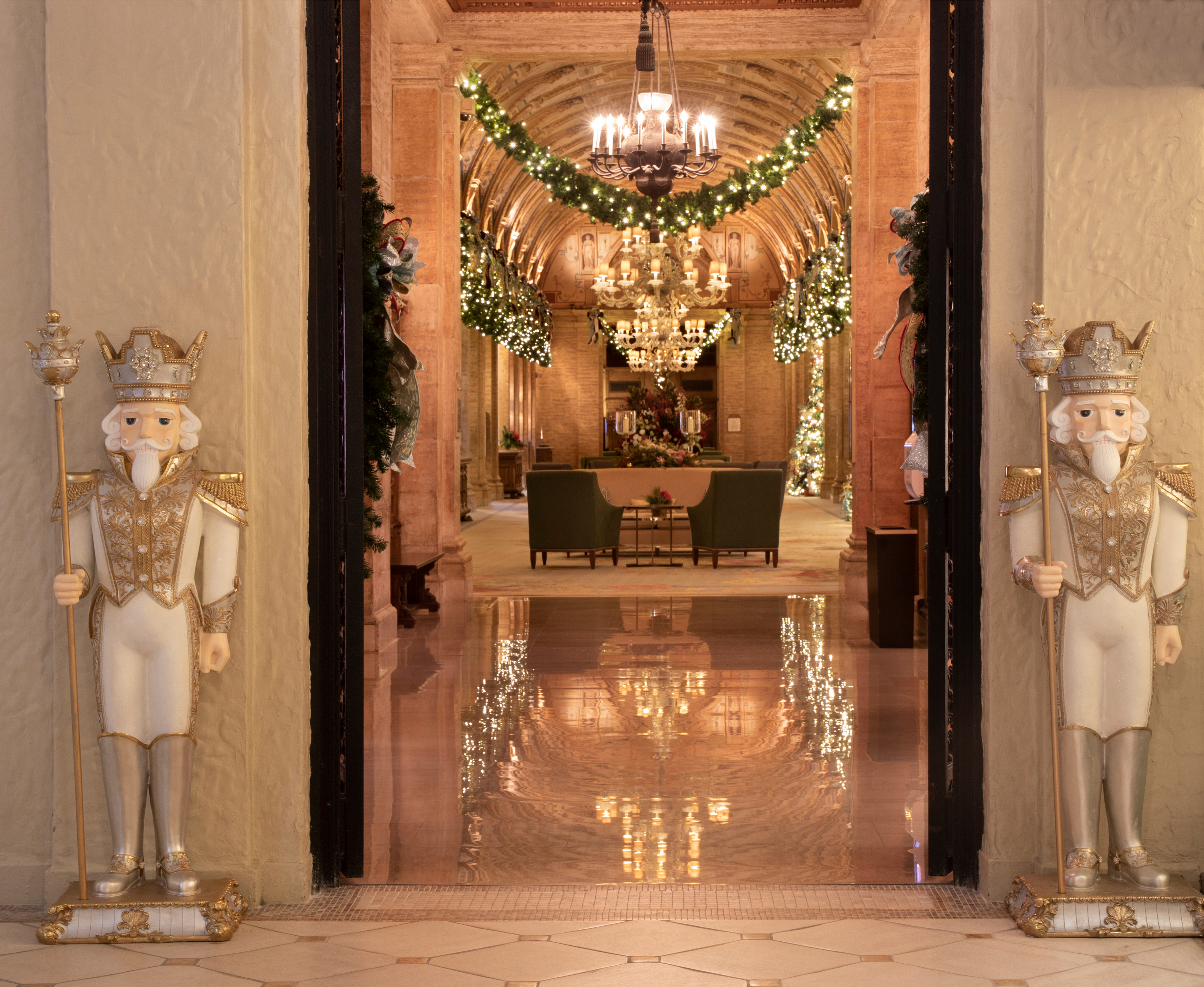 Elegant hotel lobby with gold and white nutcracker statues, chandeliers, and holiday garland decor.