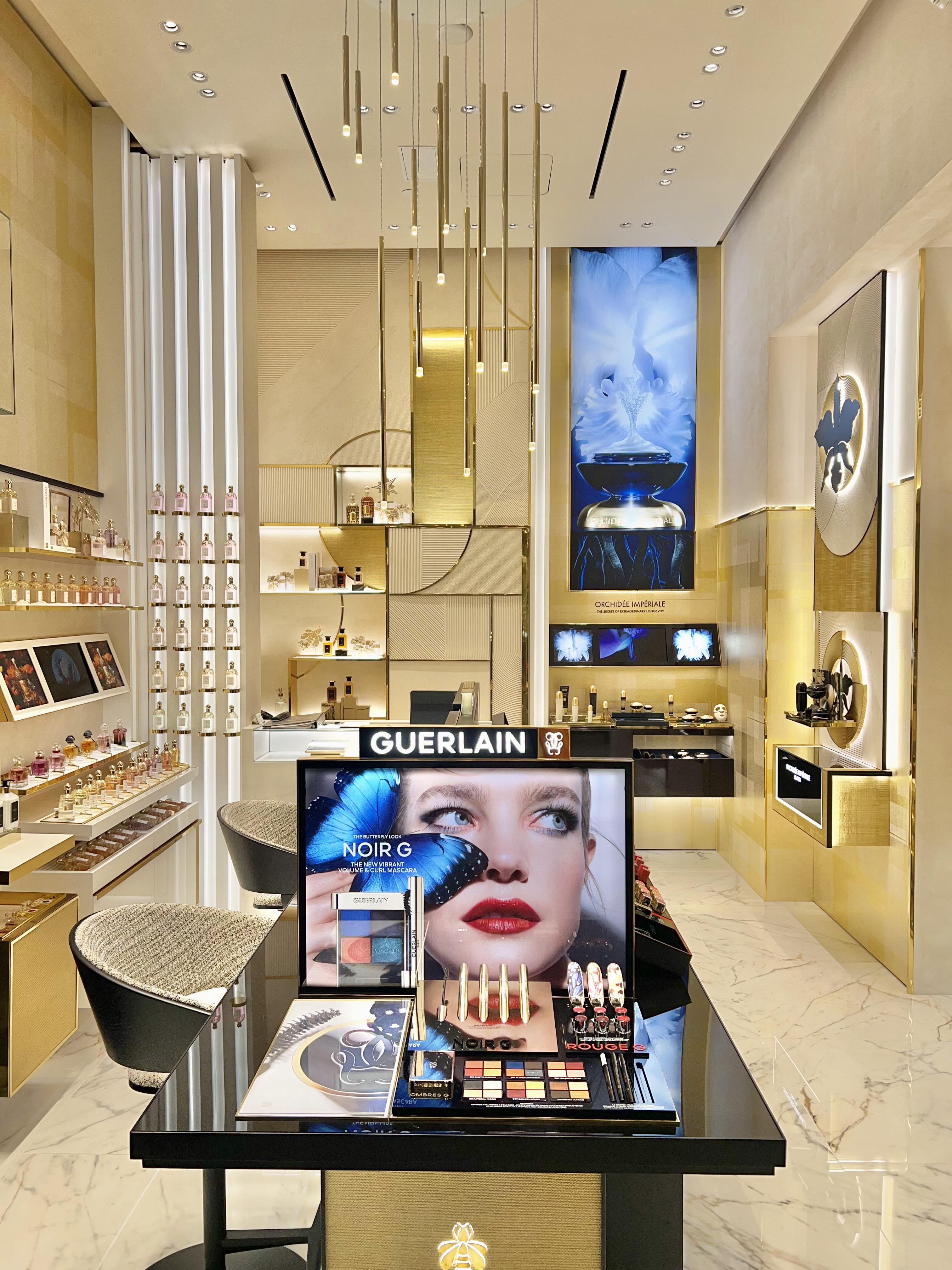 Luxury Guerlain cosmetics store interior with gold accents, pendant lights, and makeup display.