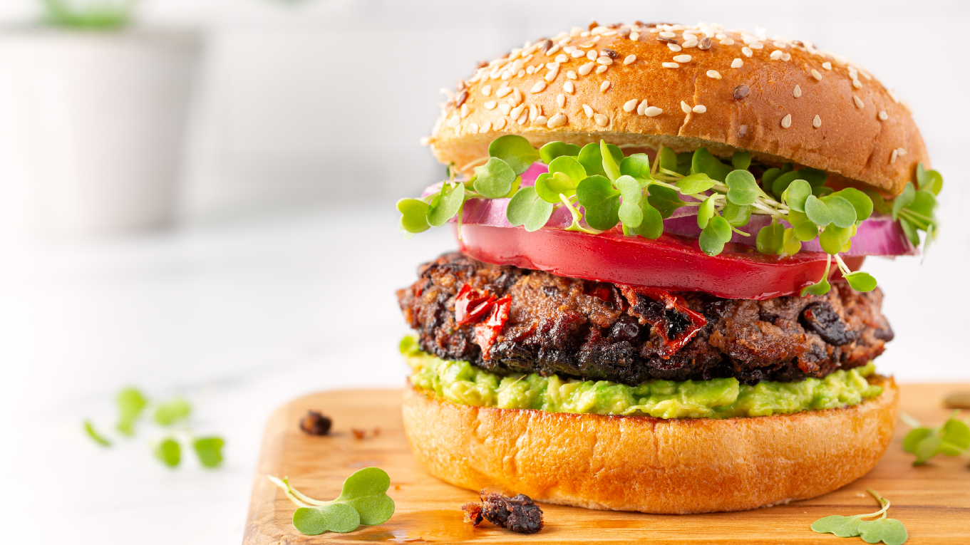 Black bean burger with a bun, avocado spread, tomato, onion, and sprouts.