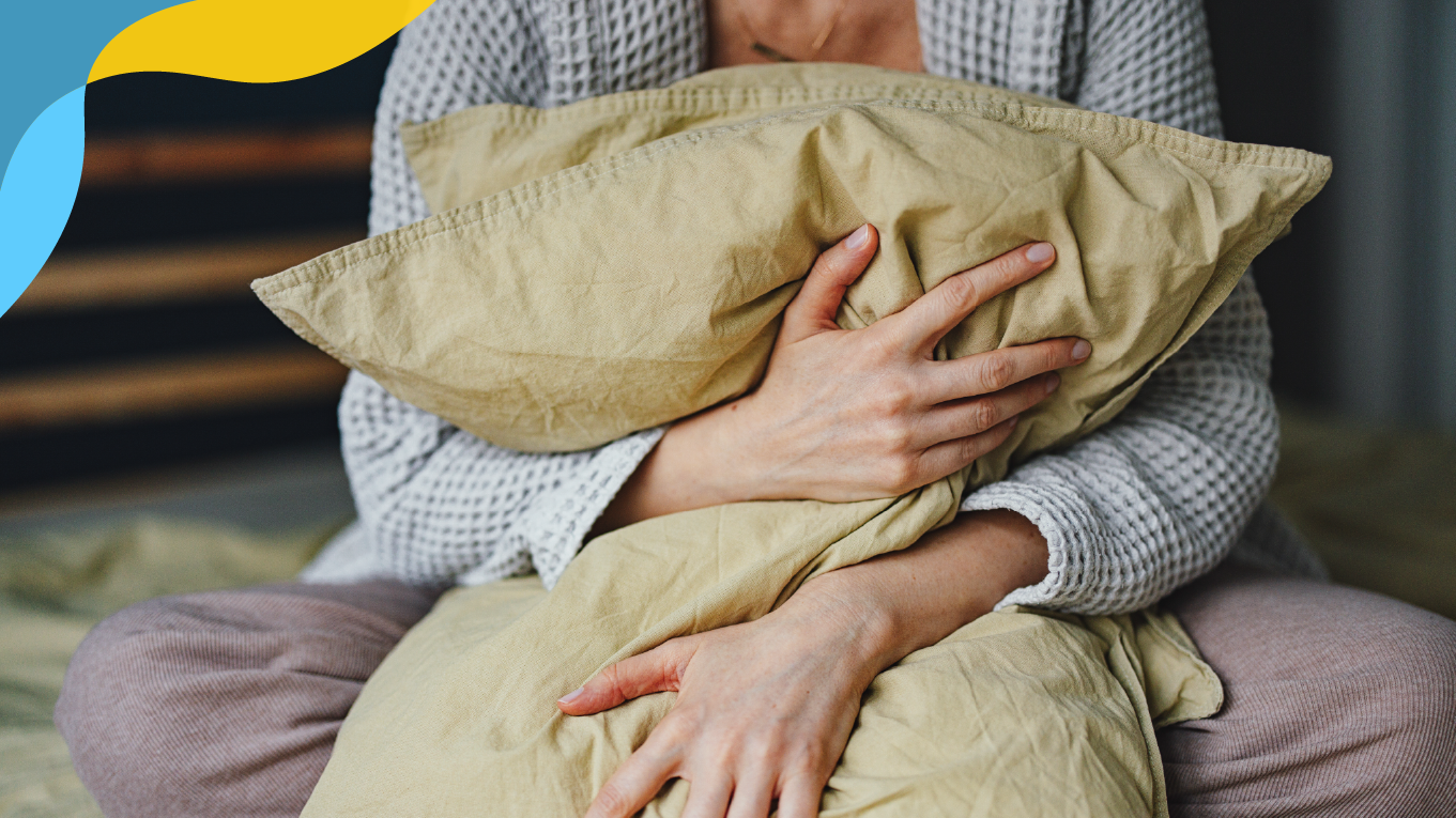 Woman clutching onto a pillow as she is sitting on her bed.