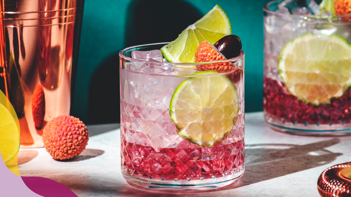 Two pink-tone cocktails with ice, garnished with limes and fruit.