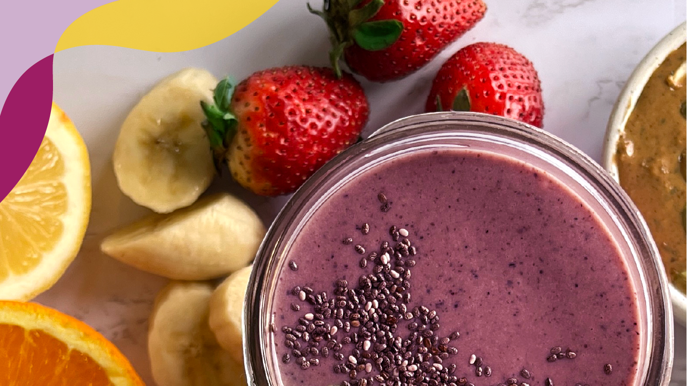 Top view of a purple-colored berry smoothie, surrounded by a lemon, orange slice, bananas, and strawberries.