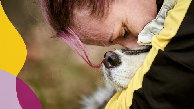Woman with pink hair kissing the top of her dog's head.