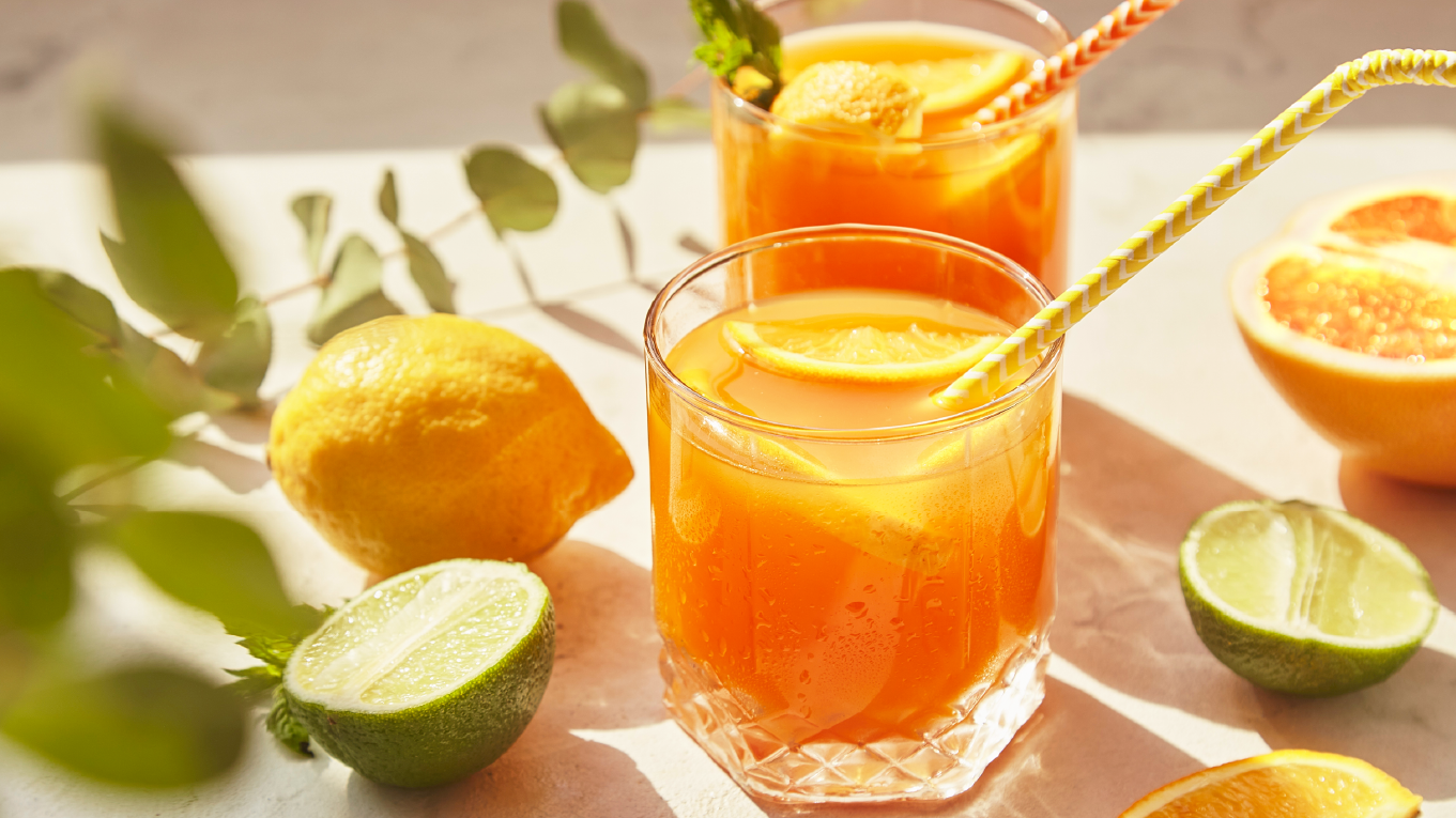 Two glasses of sparkling orange juice surrounded by orange and lime slices.