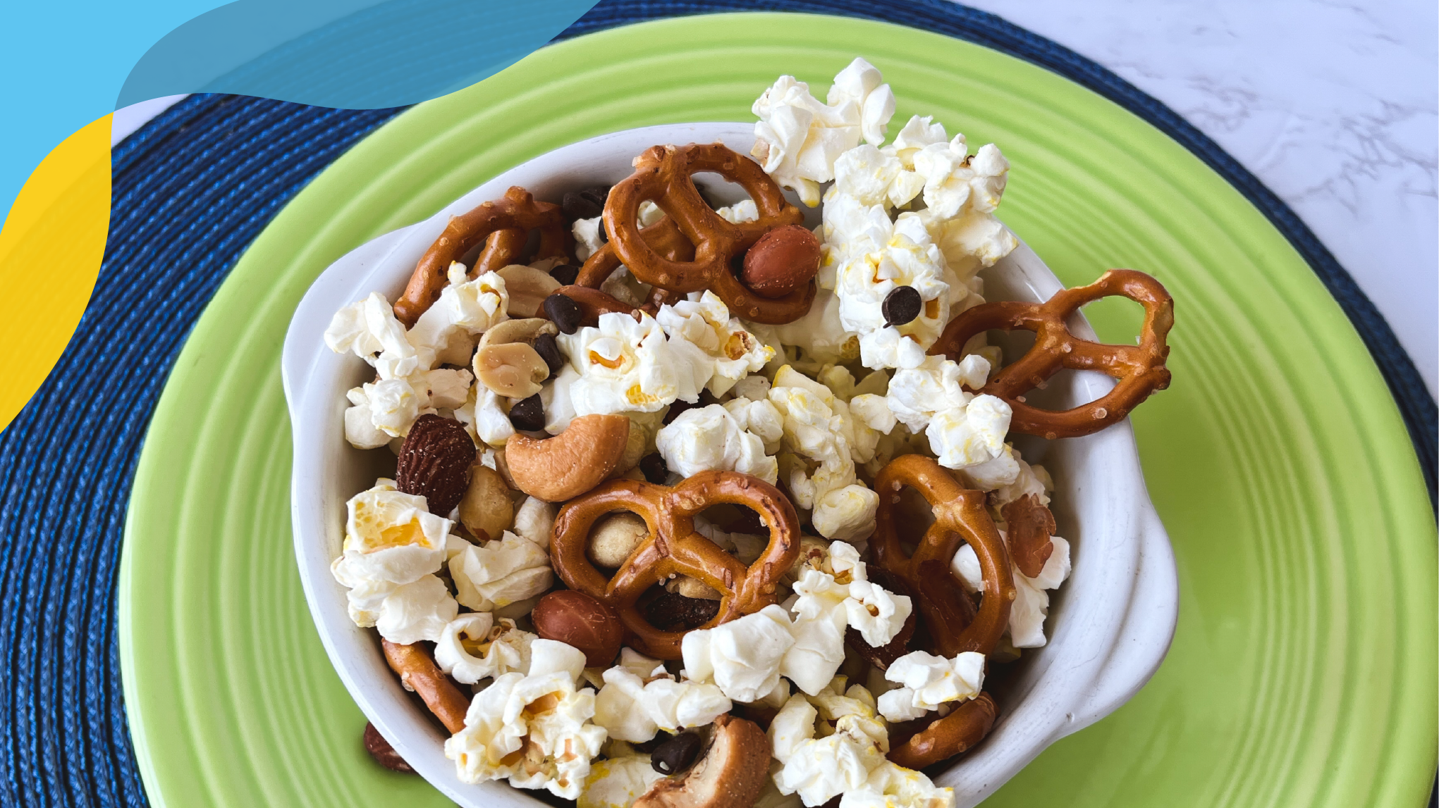 Green plate with a white bowl filled with nuts, popcorn, and pretzels.