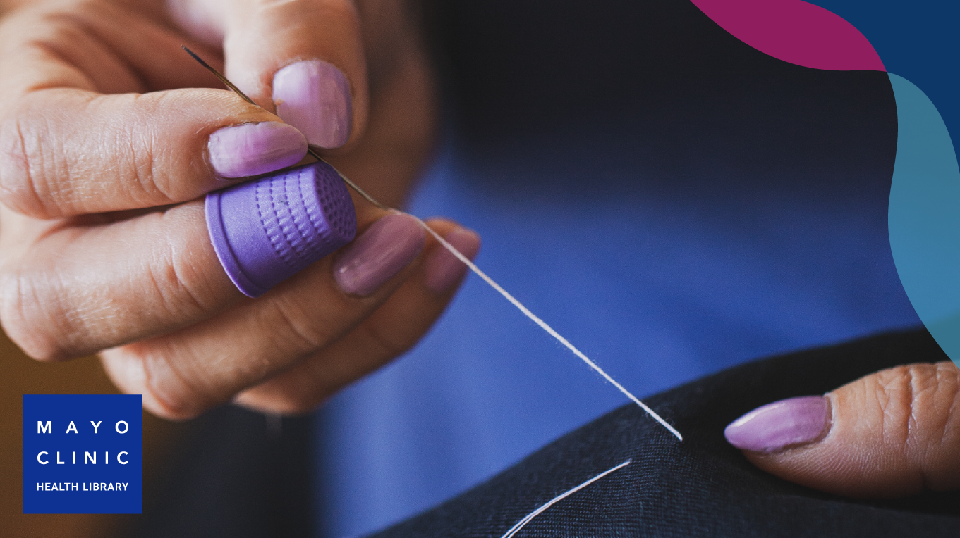 A woman with lilac-colored nail polish hand sewing with a threading needle in hand.