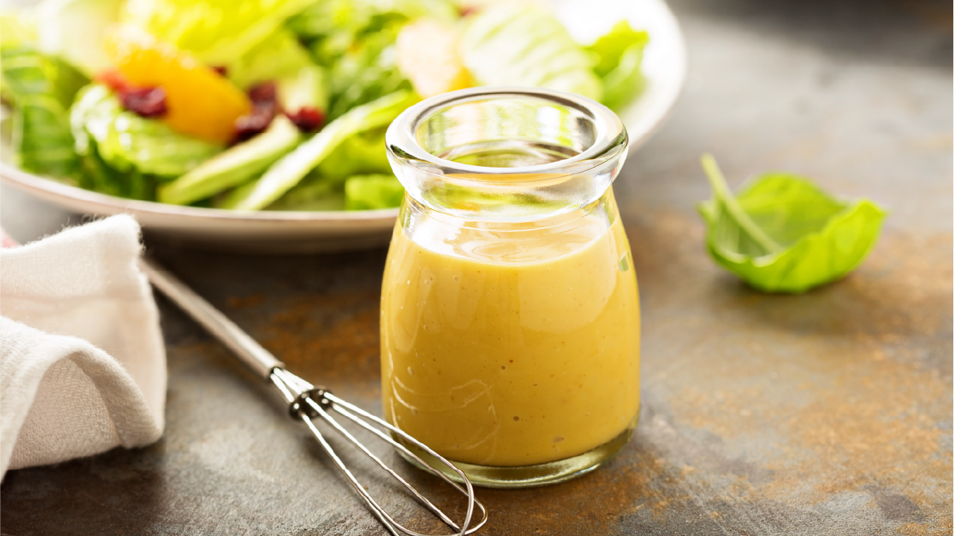 Small glass jar of golden turmeric dressing with a salad in the background.