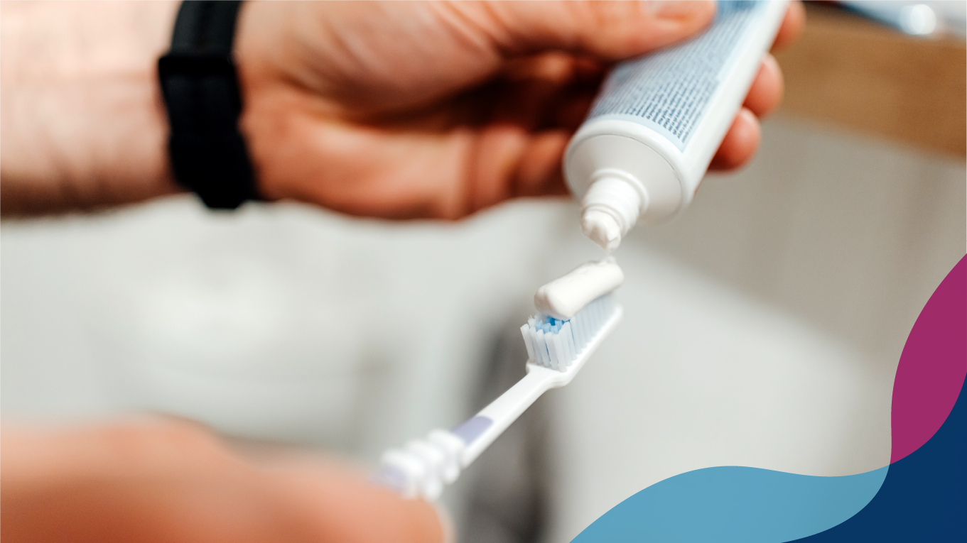 Person wearing a black watch, applying toothpaste to a toothbrush.