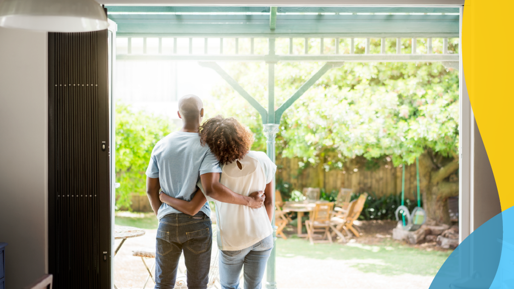 Couple looking outside with their arms wrapped around each other's back.