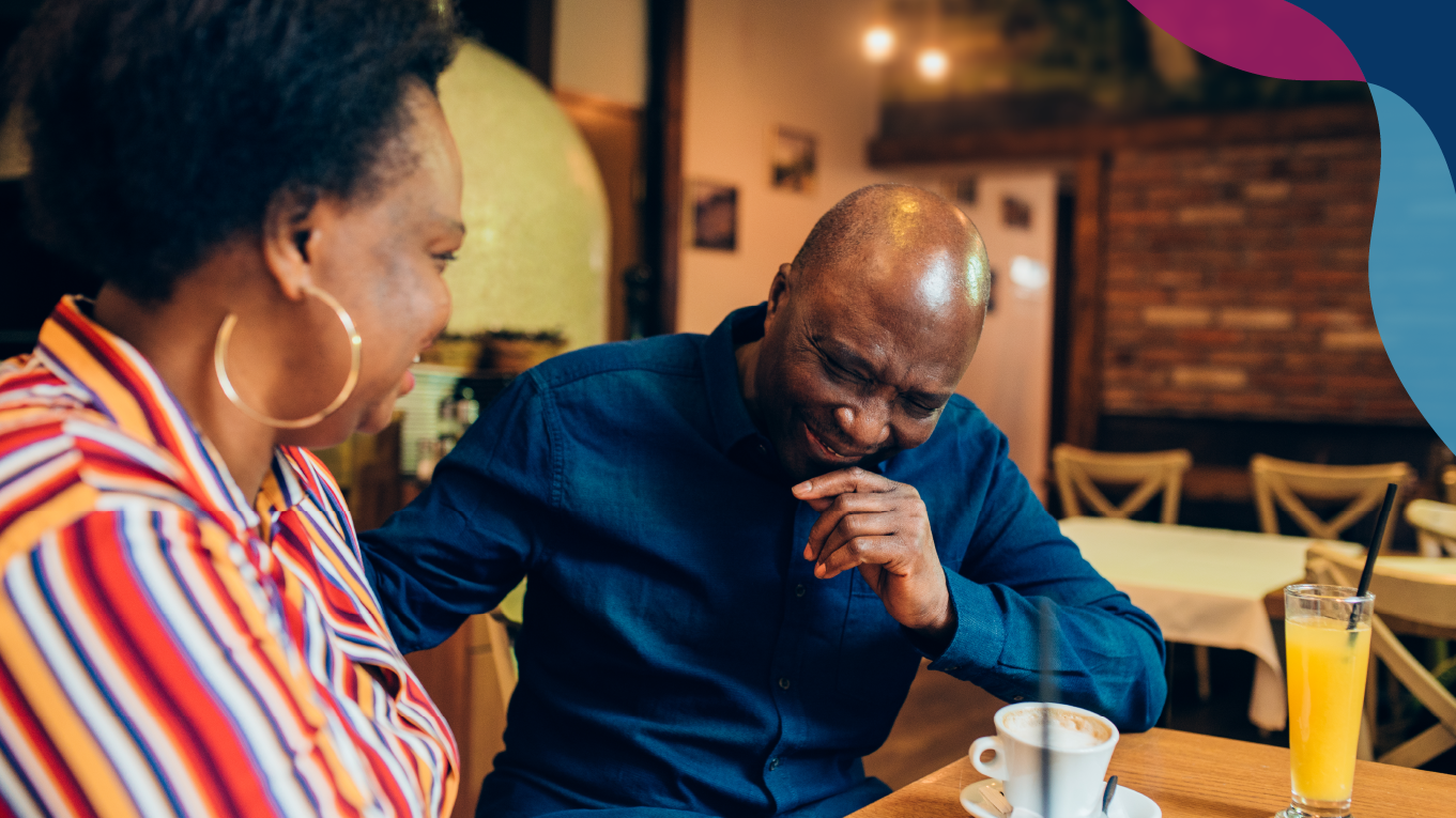 Black man and woman sitting in a coffee shop talking and smiling.