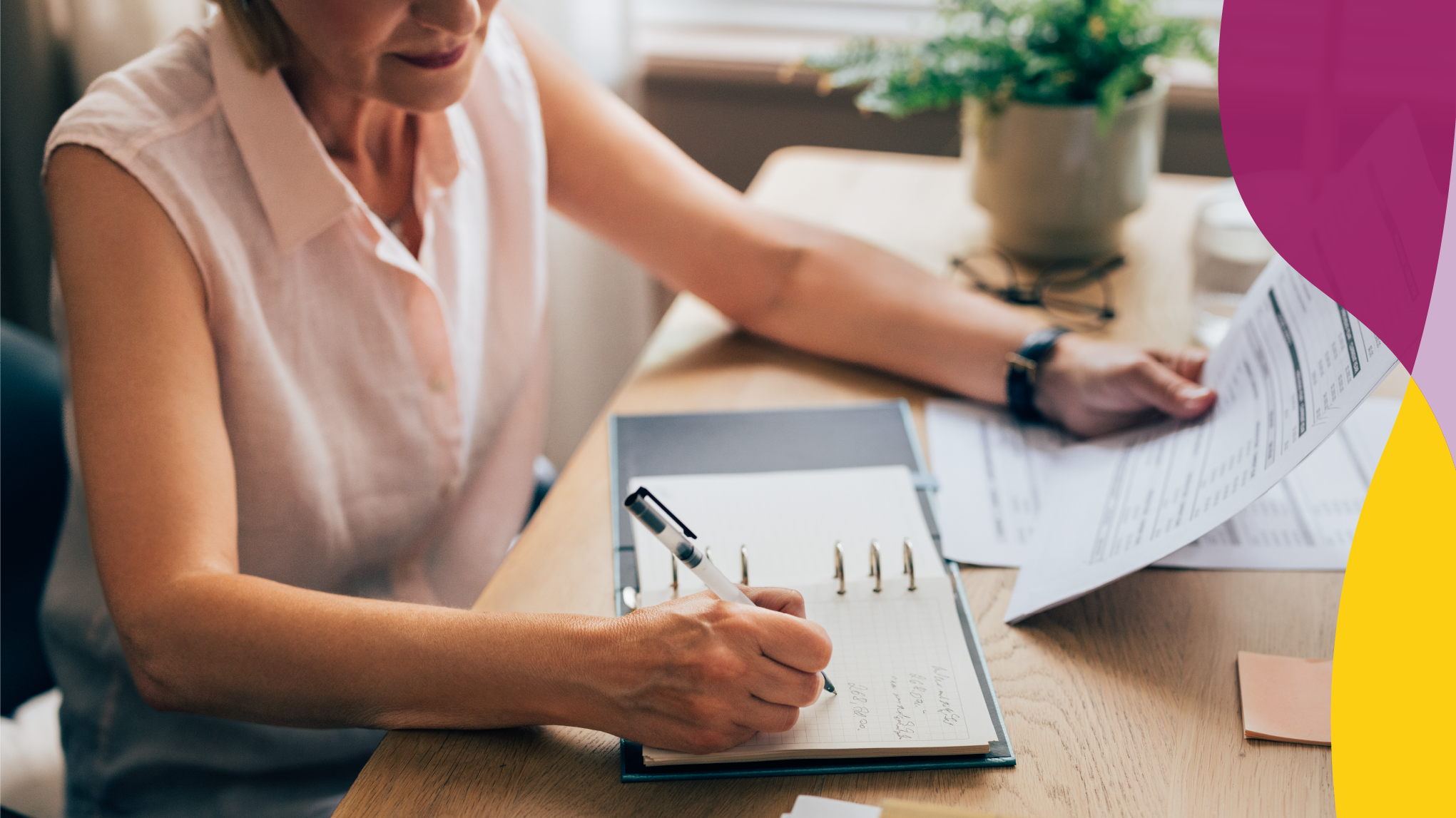 Mature woman reviewing documents at a desk with a green potted plant in the background.