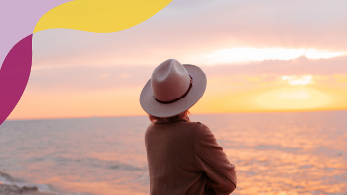 Woman in a hat looking out at the sunset.