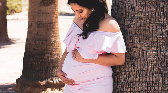 pregnant woman touching her belly against backdrop of palm trees