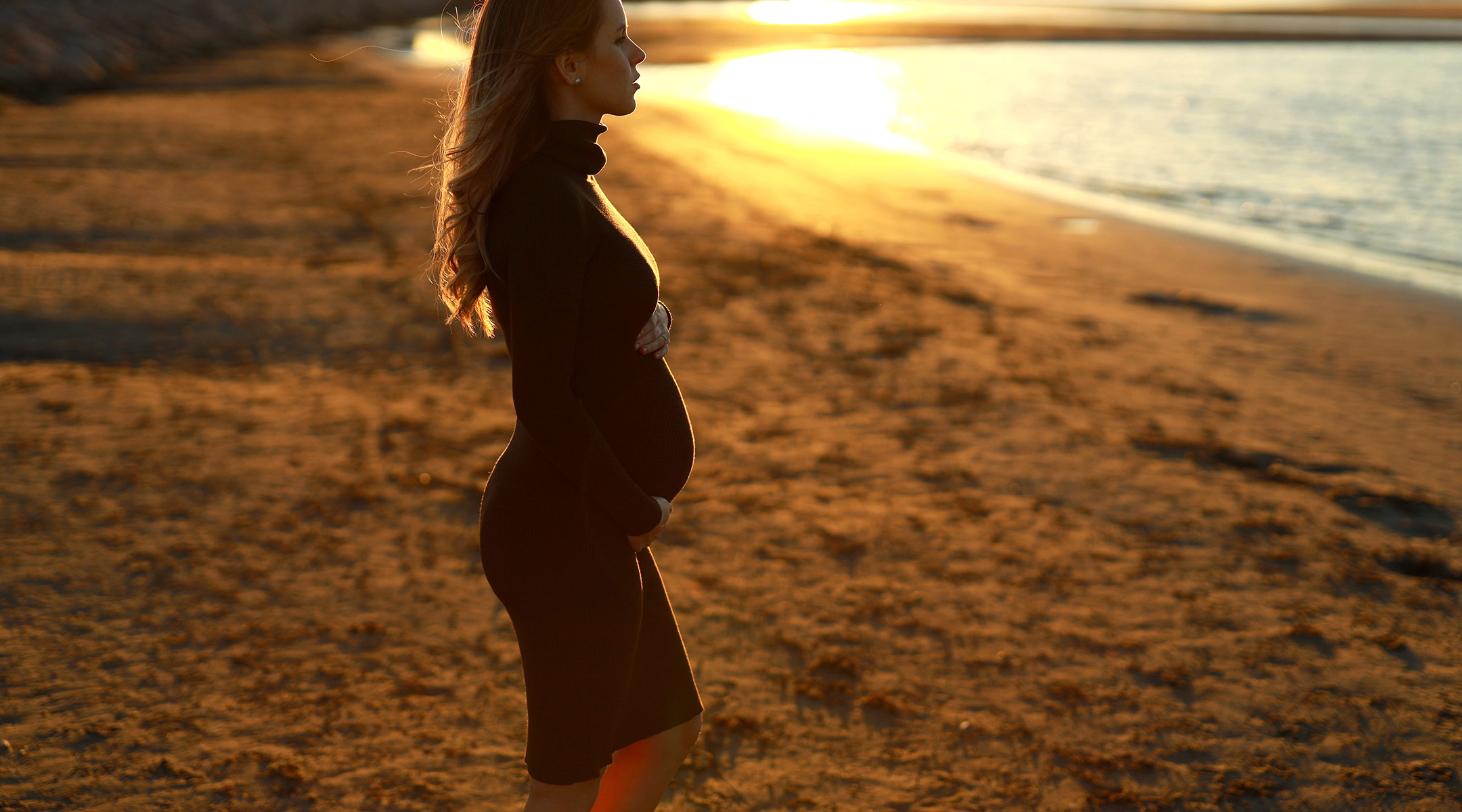 serious pregnant woman at the beach looking at the ocean
