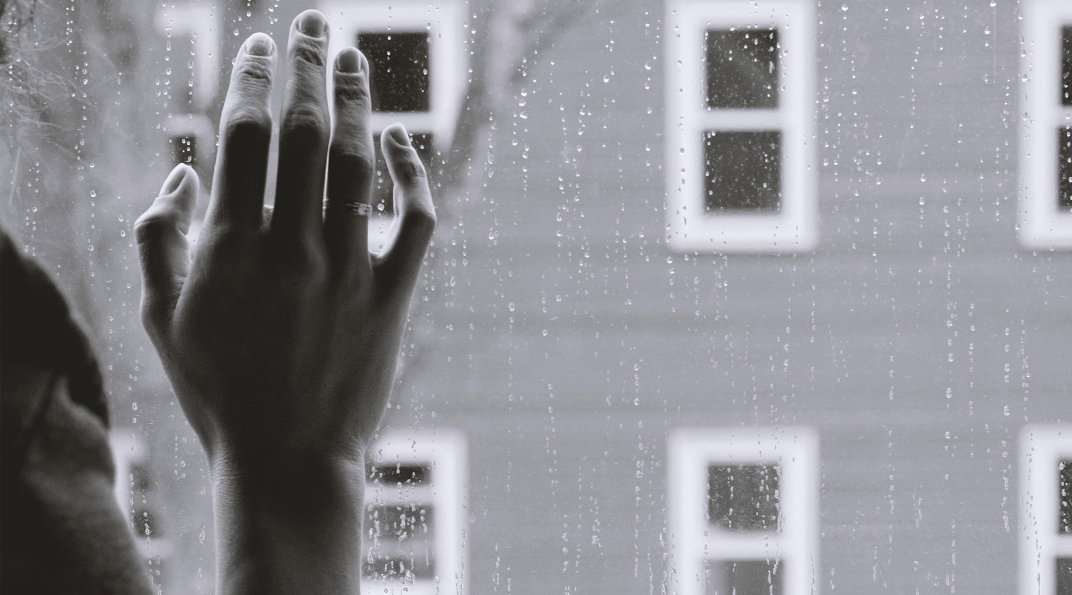 sad person holding hand to window and looking at the rain
