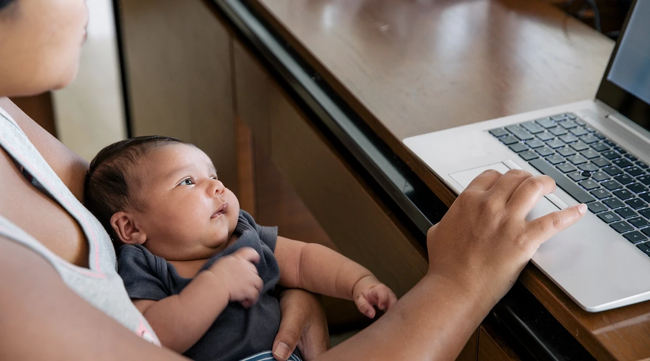 mother working on laptop while holding baby