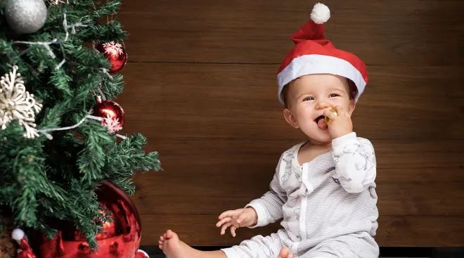baby wearing a santa hat playing with christmas tree ornaments