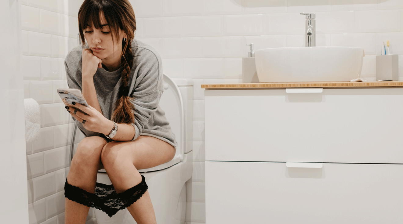 woman looking at phone while sitting on toilet in bathroom