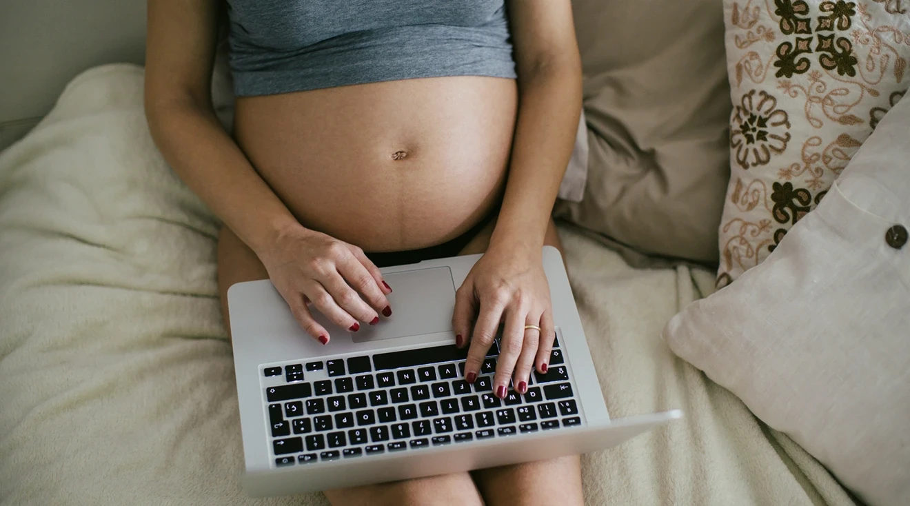 pregnant woman using laptop while laying in bed