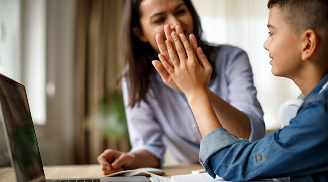 mother giving young son a high five while doing homework on laptop