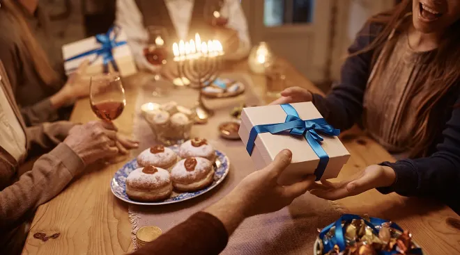 family exchanging gifts for hanukkah while sitting at the dinner table