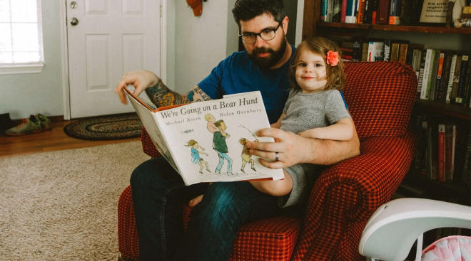 toddler sitting with her dad while reading a book
