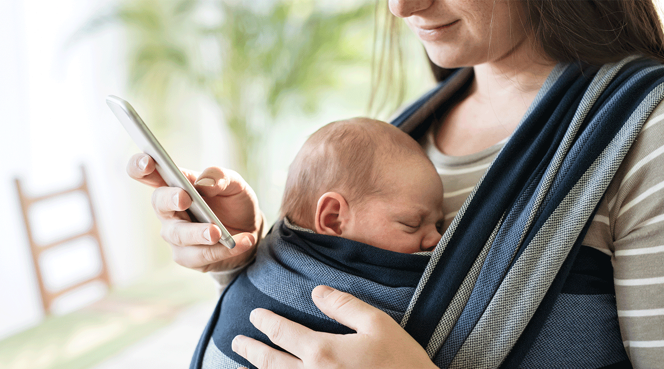 mom with baby in baby carrier and looking at phone