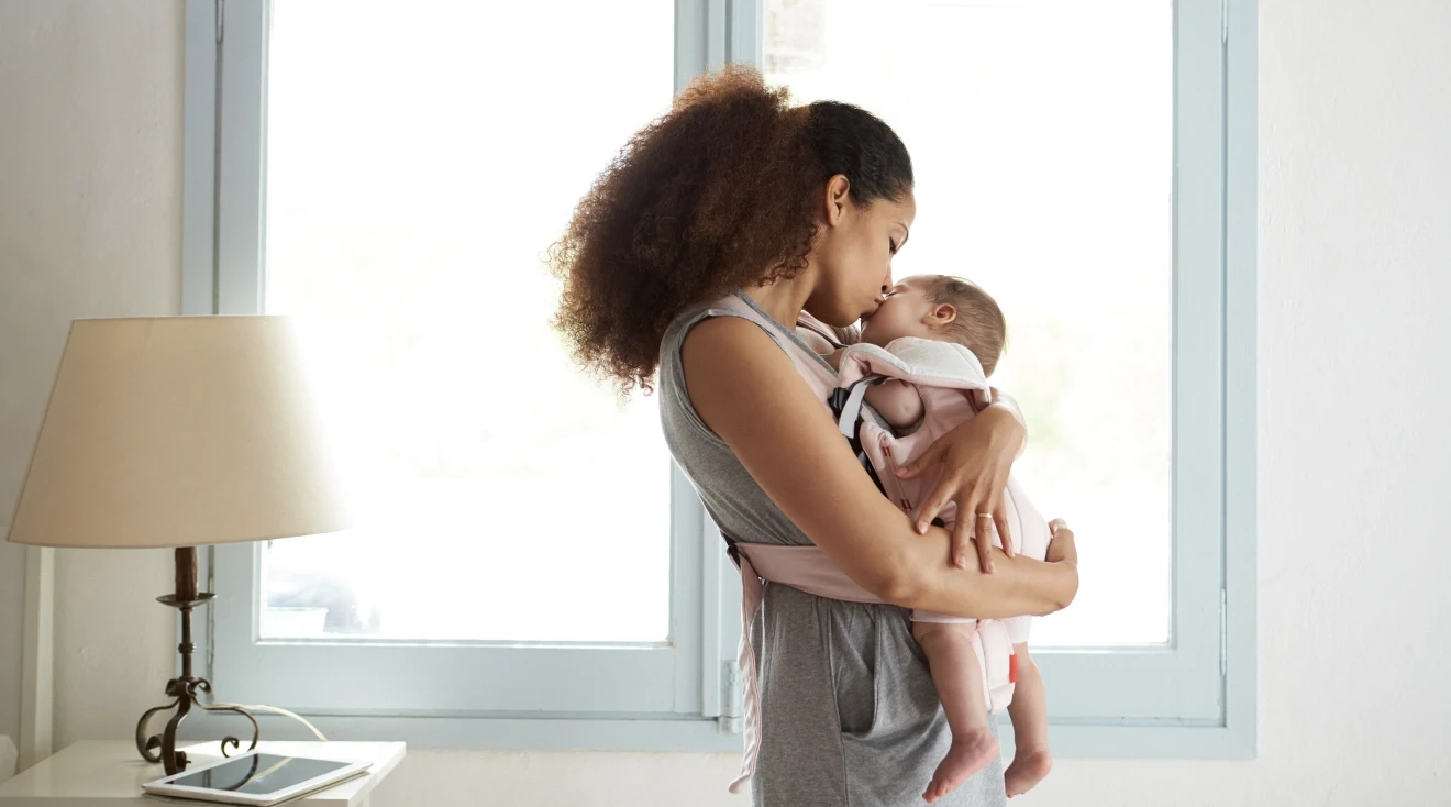 mother holding and kissing baby at home