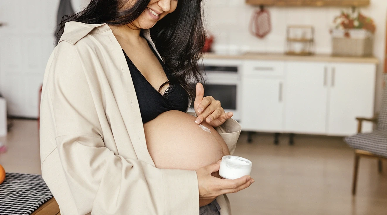 pregnant woman applying stretch mark cream onto belly