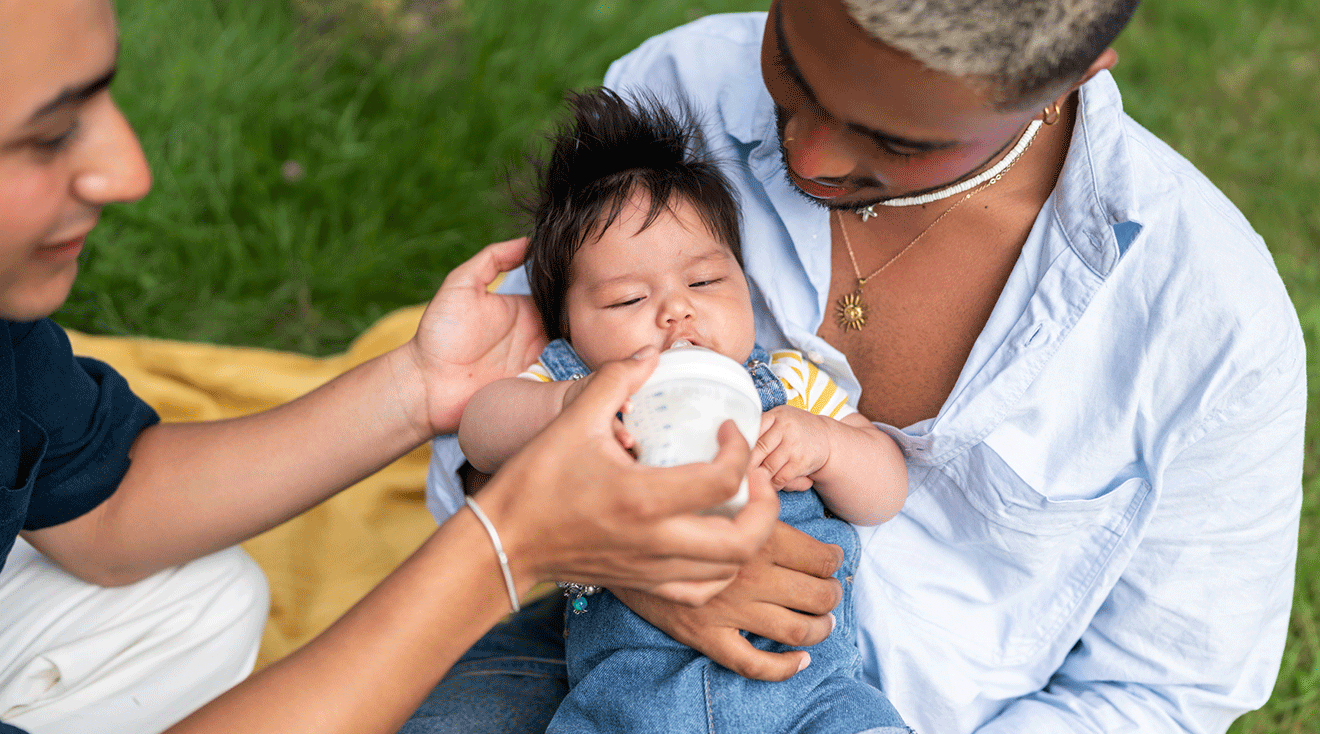 couple feeding baby from bottle in park